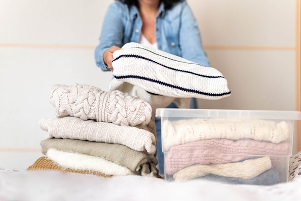 Woman stores or takes out winter sweaters from a box. Concept change of season in clothes closet