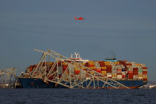 A helicopter flies over the Dali cargo vessel and the wreckage of the Francis Scott Key Bridge.