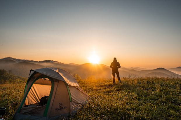 Man standing out watching the sunrise with his tent pitched in the foreground