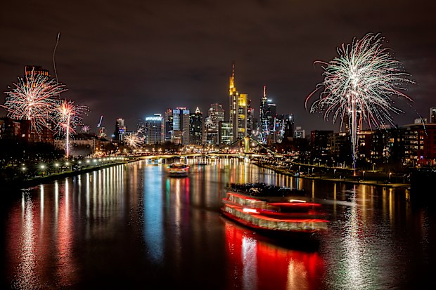 Party boats cruise over the river Main with only a few fireworks near the buildings of the banking district in Frankfurt, Germany, early Saturday, Jan. 1, 2022. 