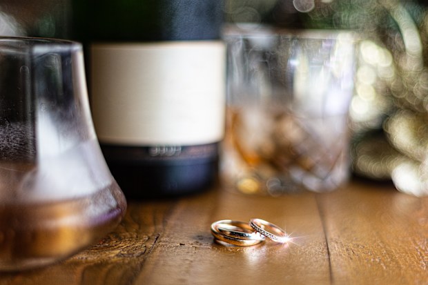 Wedding rings on a rustic wooden table with scotch and champagne in the background, out of focus.  Negative space for text or copy space,