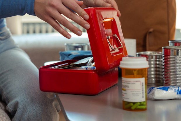 Individual preparing for emergencies with a first aid kit, canned food, and medication.