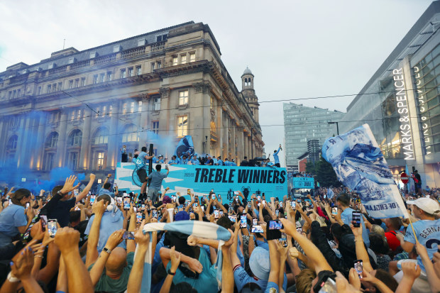 Manchester City celebrate on the open top bus as fans line the streets.