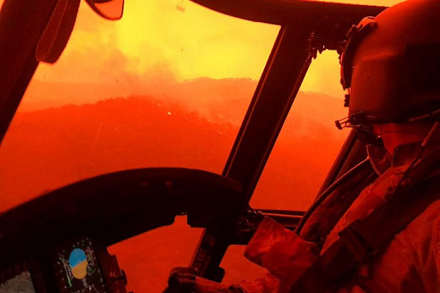 A photograph from inside a helicopter, as it flies above flames and smoke.