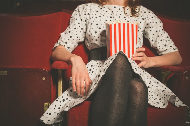Young woman sitting alone in a cinema with a bucket of popcorn.