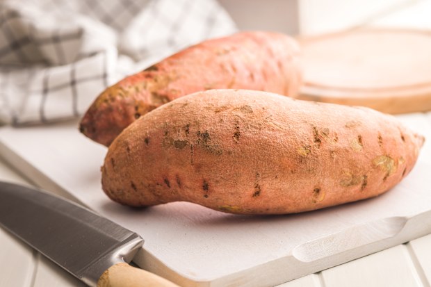 Raw sweet potatoes on cutting board on a white table.