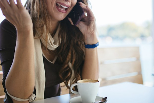 Young stressed woman freelancer talking on mobile phone at cafeteria