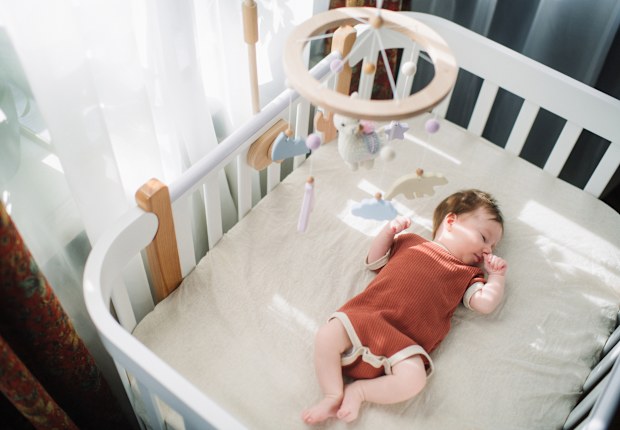 Newborn girl lies in white cradle with mobile above