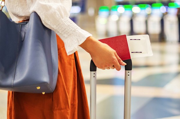 close up of unrecognizable female passenger at check-in counter in airport terminal, with luggage and passport