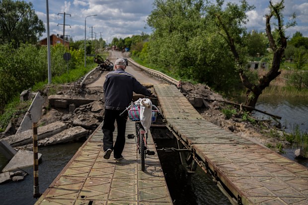 A man pushes his bicycle across a repaired bridge in Vilkhivka, outside Kharkiv, in eastern Ukraine, Friday, May 20, 2022. (AP Photo/Bernat Armangue)