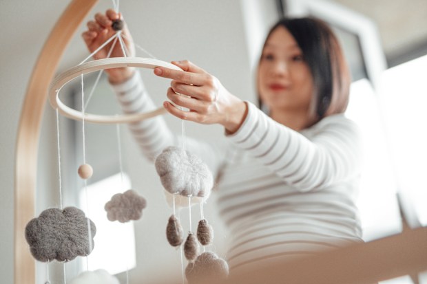Pregnant woman hanging mobile over cot in nursery