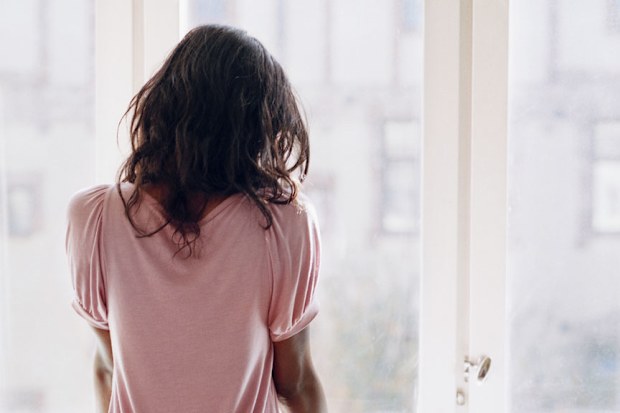 Young woman looking out window sadly