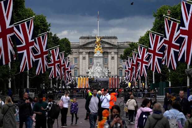 People stand on The Mall looking towards Buckingham Palace and the Queen Victoria Memorial statue as the road is lined with Union flags and closed to traffic ahead of Britain's Queen Elizabeth II's Platinum Jubilee, in London, Tuesday, May 31, 2022. 