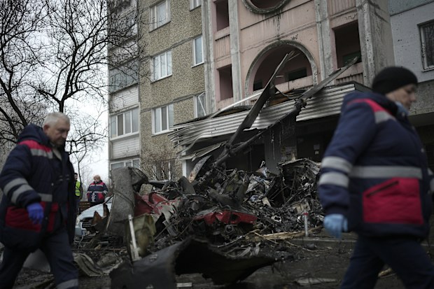 Workers pass the scene where a helicopter crashed on civil infrastructure in Brovary, on the outskirts of Kyiv, Ukraine, Wednesday, Jan. 18, 2023 