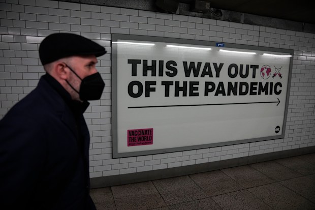 A man wearing a face mask to curb the spread of coronavirus walks past a health campaign poster from the One NGO, in an underpass leading to Westminster underground train station, in London, Thursday, January 27, 2022. 
