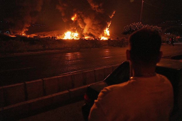 A man looks at flames rising from an oil storage facility after it appeared to have been struck by an Israeli strike in Tehran