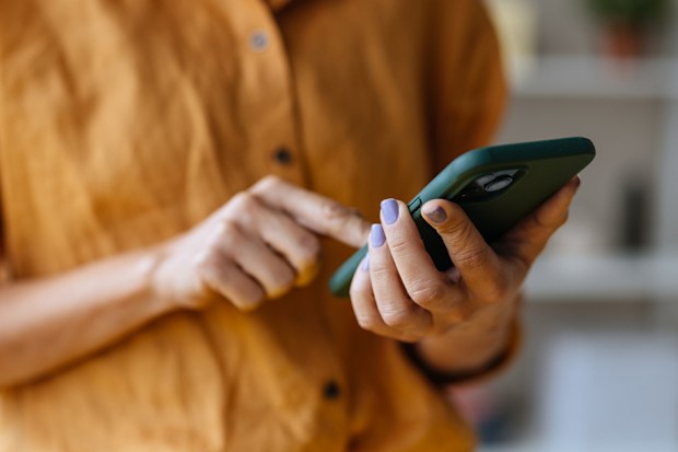 A close up view of an unrecognizable Caucasian entrepreneur texting on her smartphone while standing indoors.