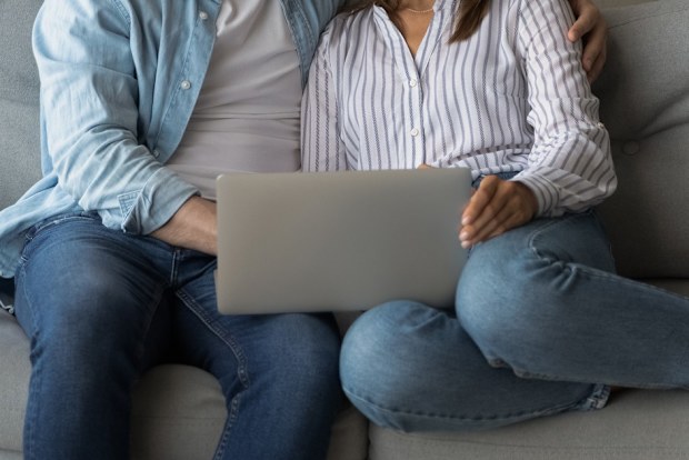 man and woman sitting on lounge looking at laptop screen