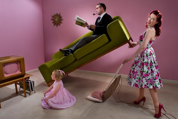 Wife vacuuming while husband relaxes