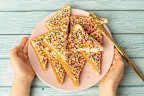 Young female hands holding Fairy Bread written with fairy bread on a plate on a blue background.�