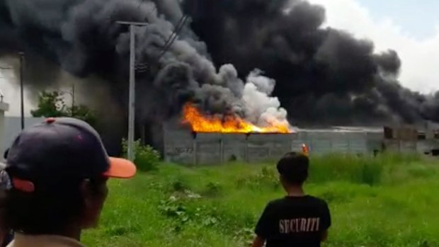 Residents watch as thick black smoke billows from the site of the explosion at a firecracker factory in Tangerang. (AAP)