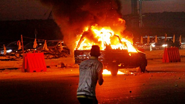 A man watches on as a vehicle burns during a riot outside the Air Defense Stadium in a suburb east of Cairo. (AAP)