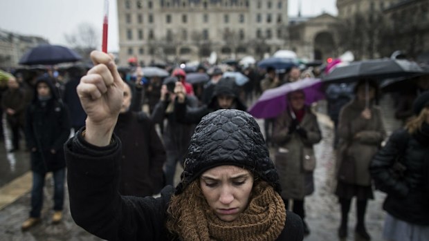 A young woman holds aloft a symbolic people as she joins others gathered for a minute of silence in front of Notre Dame cathedral. (AAP)