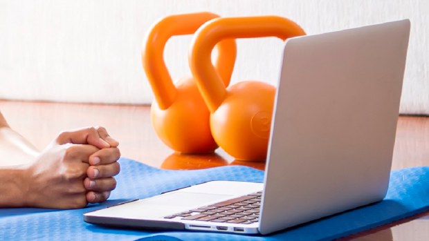 Young woman doing yoga excercise with online app on computer laptop in her living room at home.
