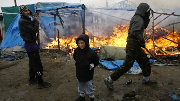Migrants stand in front of a burning dwelling in a makeshift migrants camp near Calais. (AAP)