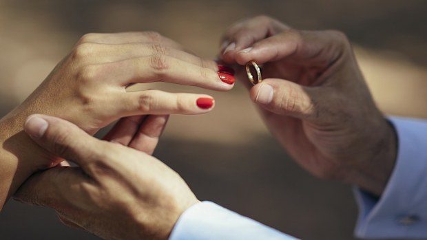 Groom putting wedding ring on finger of bride, close up