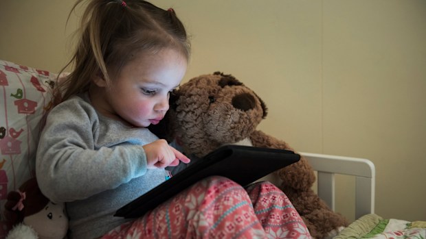 A toddler plays with a touchscreen device in her bed. (AFP)
