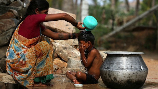 An Indian woman bathes her kid to beat the heat in Gauribidanur village. (AAP)