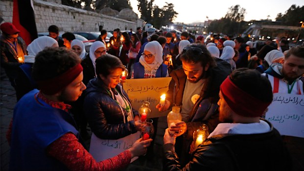 Syrians holding posters reading, 'we want peace.. we love peace' and pictures of Syrian President Bashar Assad during a vigil at the Ummayyad Square in Damascus. (AAP)