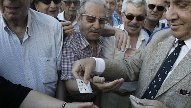 A bank employee distributes priority tickets to pensioners customers as they wait outside a National Bank of Greece in Athens. (AAP)