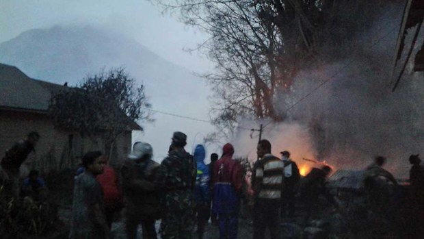Villagers and rescuers stand near a burning tree after it was hit by pyroclastic flows from the eruption of Mount Sinabung. (AP)