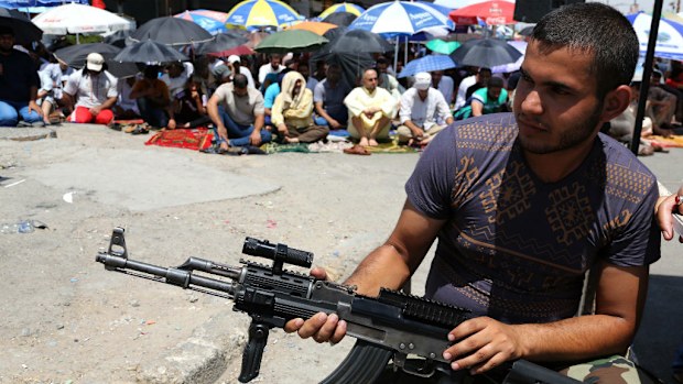 A Shiite fighter stands guard next to followers of Shiite cleric Muqtada al-Sadr attending open-air Friday prayers in the Shiite stronghold near Baghdad. (AAP)