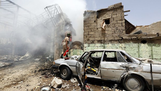 A member of the Houthi militia carrying a fire extinguisher stands outside a shop destroyed in an airstrike. (AAP)