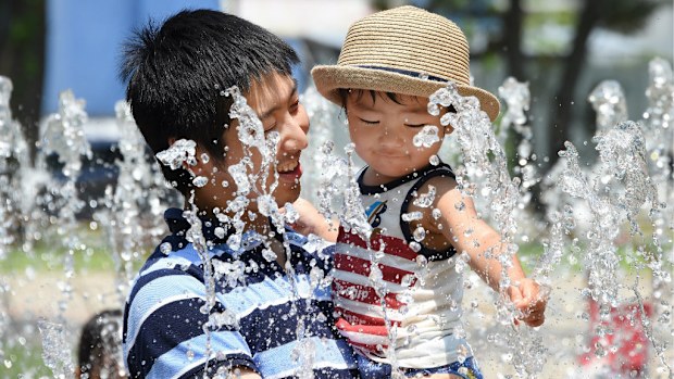 A father and son bathe in a fountain in a Tokyo park to stave off the worst of the summer heat. (Getty)