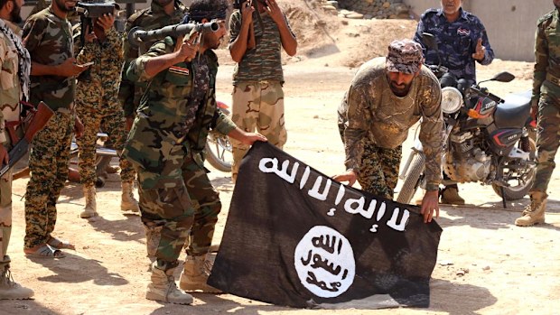 Iraqi security forces hold a flag of the Islamic State group they captured during an operation outside Amirl on September 1. (AAP)