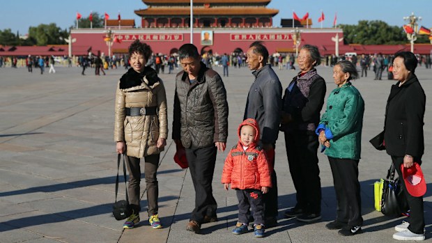 A child stands beside a group of people as they wait to take group photos on Tiananmen Square.