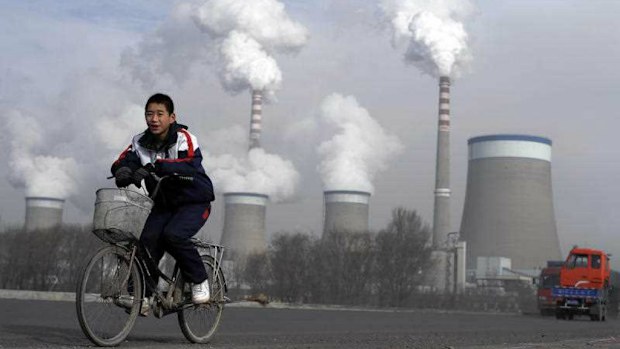 A Chinese boy cycles past a cooling towers of a coal-fired power plant in Dadong, Shanxi province, China. (AP)