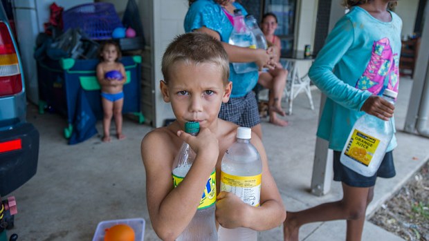 Haywen Kulka, aged 5, helps fill empty bottles with fresh water as his family plans to sit out Cyclone Nathan in their bessa block house in Cooktown. (AAP)