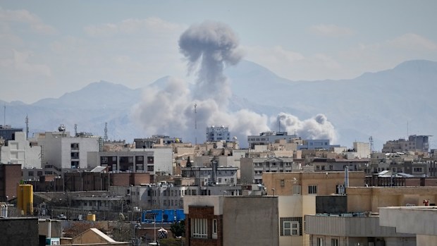 People watches from rooftop as a plume of smoke rises after a strike in Tehran, Iran, Sunday, March 1, 2026. (AP Photo/Vahid Salemi)