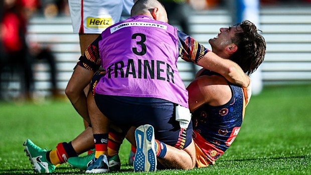 Josh Rachele of the Crows is held by a trainer after injuring his knee.