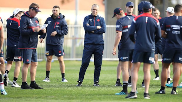 Michael Cheika looks on as Roosters coach Trent Robinson gives instructions to the players.