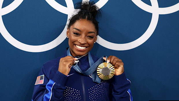 Simone Biles shows off a gold medal and a goat pendant.