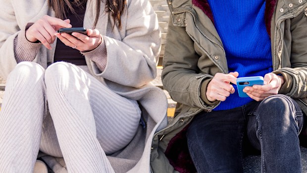 three unrecognizable friends sitting in the floor scrolling together through social media with mobile phone, concept of friendship and modern lifestyle
