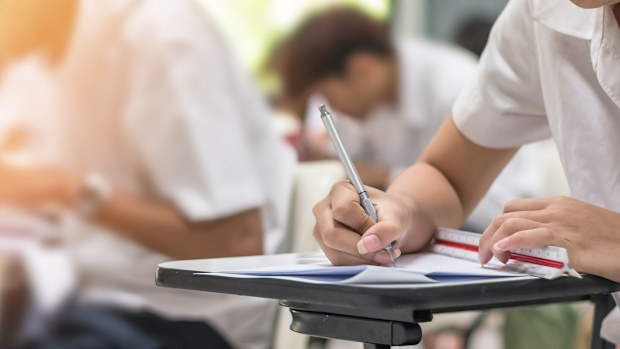 Exam at school with student's taking educational admission test in class, thinking hard, writing answer in university classroom, education and world literacy day concept