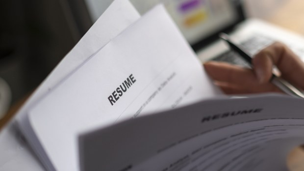 A shadowy photo of hands flipping through printed out resumes with a laptop open in the background.
