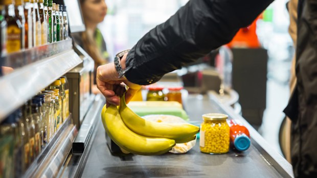 A person putting some bananas and other groceries on the conveyor at a store checkout.